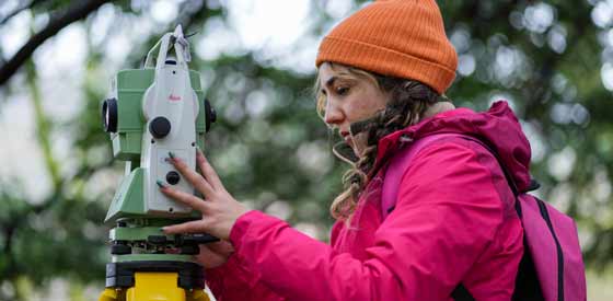 Female outside looking through a measuring tool that has a camera lens on it