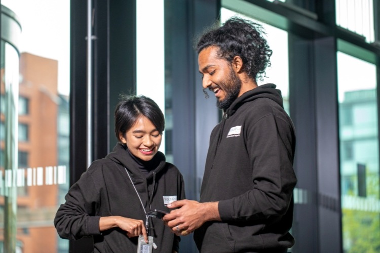 Two students chatting while looking at a phone in Manchester’s Nancy Rothwell Building.