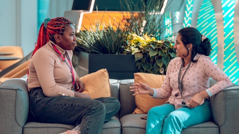 Manchester researchers, Chithra and Leona, chatting on a sofa in a foyer at the Henry Royce Institute.