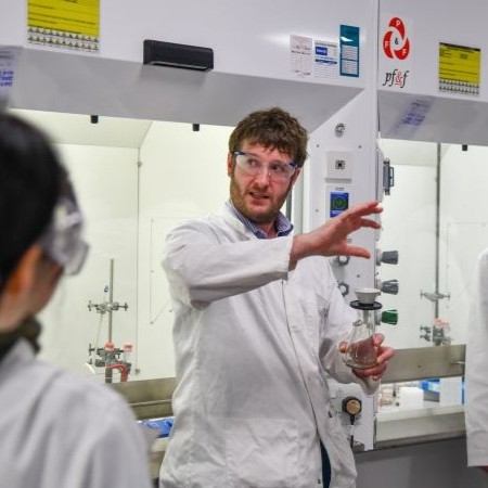 Person in lab coat explaining an experiment to a group in a University of Manchester lab.